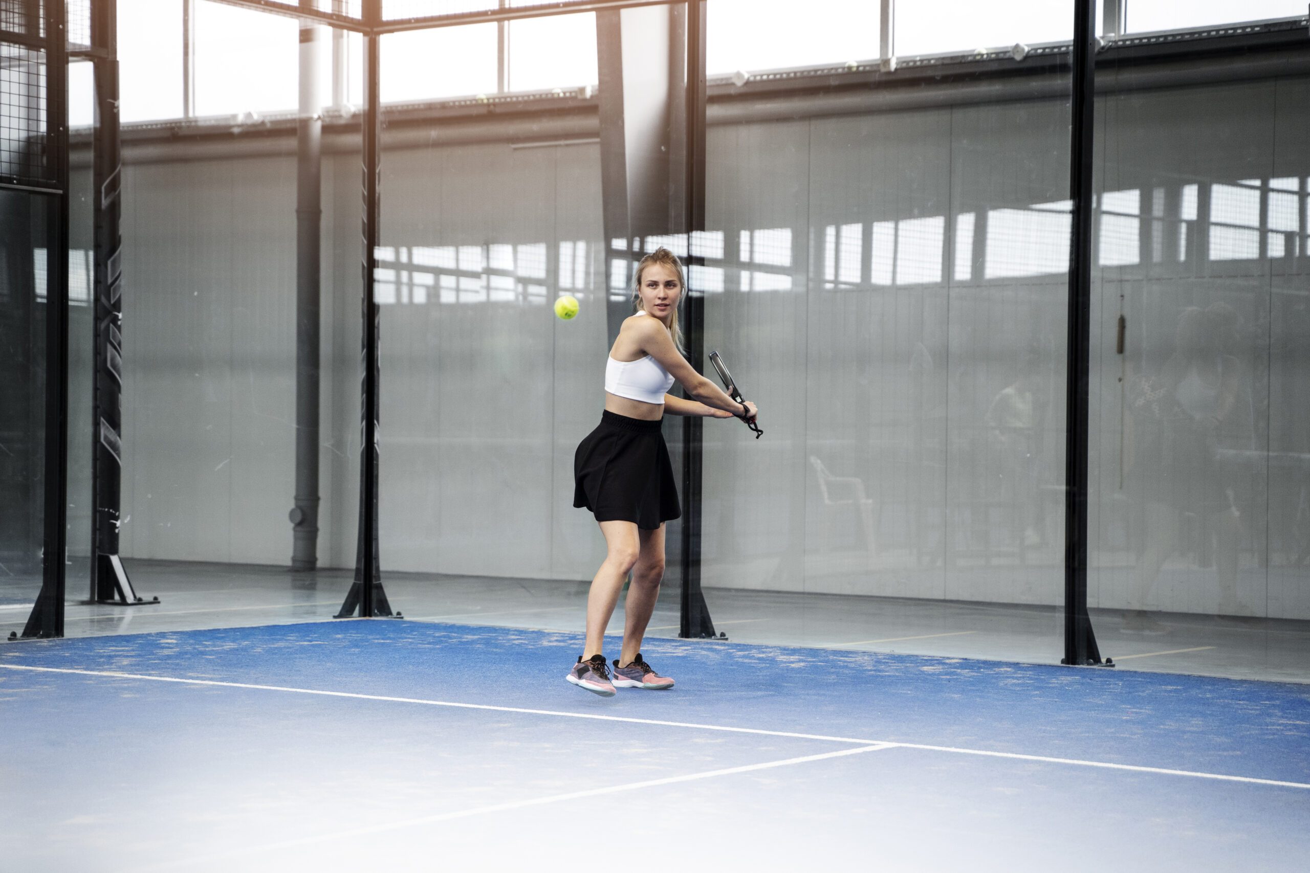 Une joueuse de padel prête à frapper la balle sur un terrain couvert